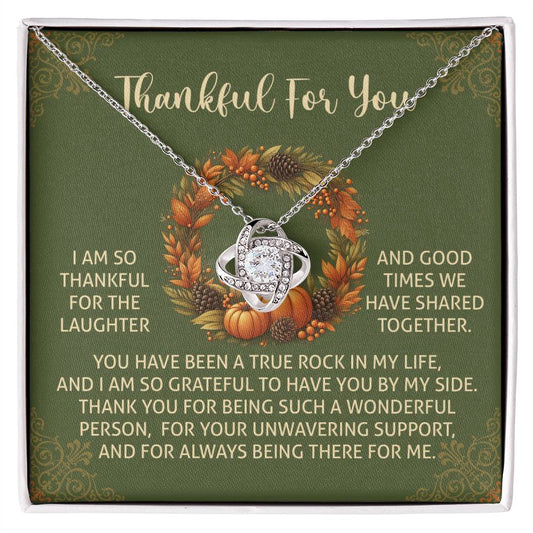 The Thanksgiving-By My Side - Love Knot Necklace is presented in a gift box with a heartfelt message. This exquisite design, decorated with delicate cubic zirconia crystals, sits against a green background framed by a floral wreath, making it an ideal personalized gift for someone special.