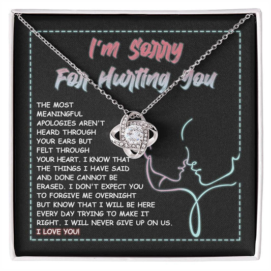 A 14k white gold Sorry-Never Give Up - Love Knot Necklace with an interlocked pendant set with cubic zirconia crystals sits on a note that reads, "I'm sorry for hurting you," accompanied by an apology message expressing regret, commitment to make things right, and affirming love.