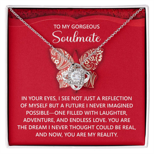 The Soulmate-My Reality - Love Knot Necklace, adorned with cubic zirconia crystals and a butterfly pendant, comes elegantly displayed in a box. It includes a romantic message for your soulmate on white text over a red background, completing this personalized gift.