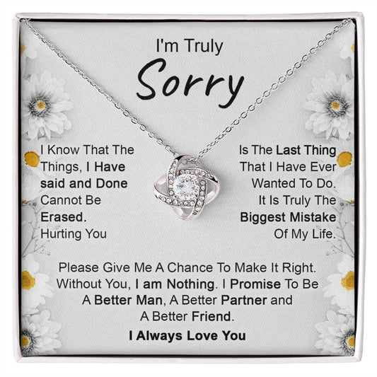 The "I’m Truly Sorry - Love Knot Necklace," featuring a pendant adorned with cubic zirconia crystals, rests on a heartfelt message that reads, "I'm Truly Sorry." The text conveys remorse for past actions and a commitment to becoming a better person, partner, and friend. The background is decorated with delicate floral designs.