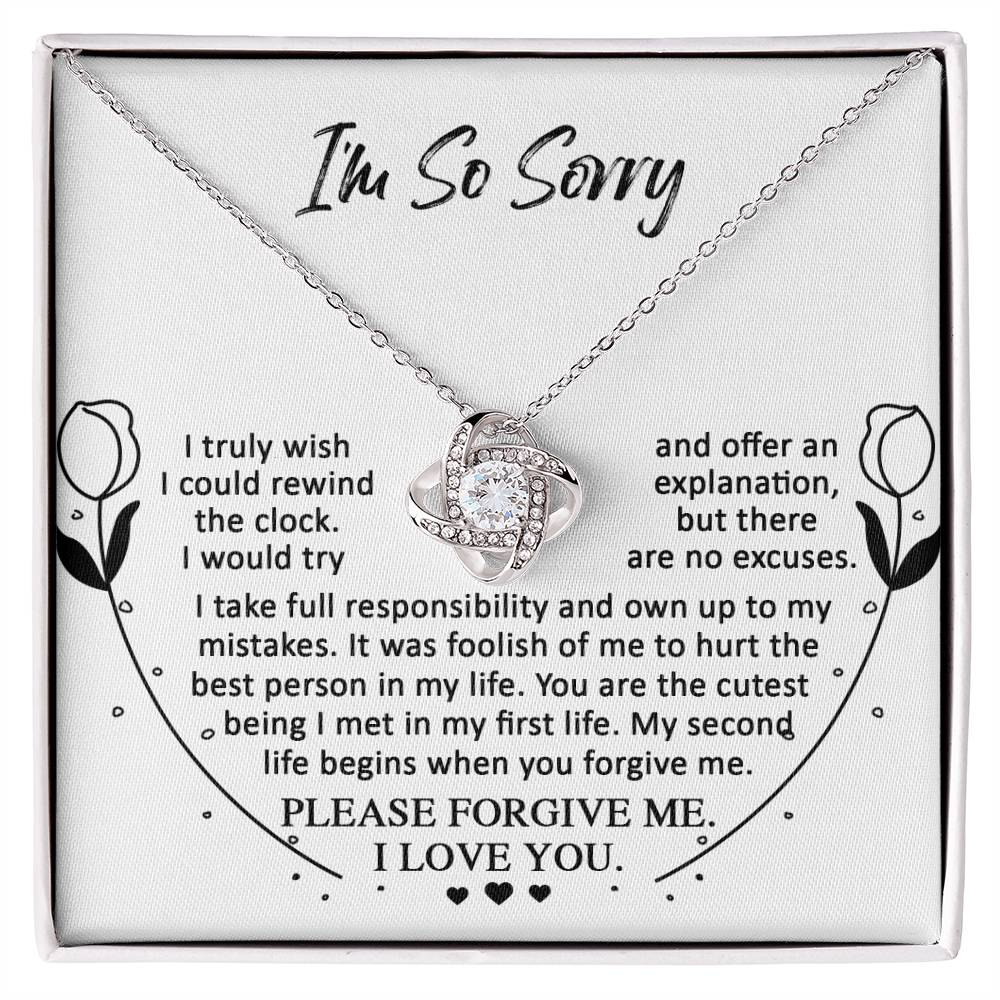 The "Sorry-My First Life - Love Knot Necklace" showcases a dazzling heart-shaped pendant encircled by an apologetic and loving message, elegantly embellished with floral decorations on either side and sparkling Cubic Zirconia Crystals.