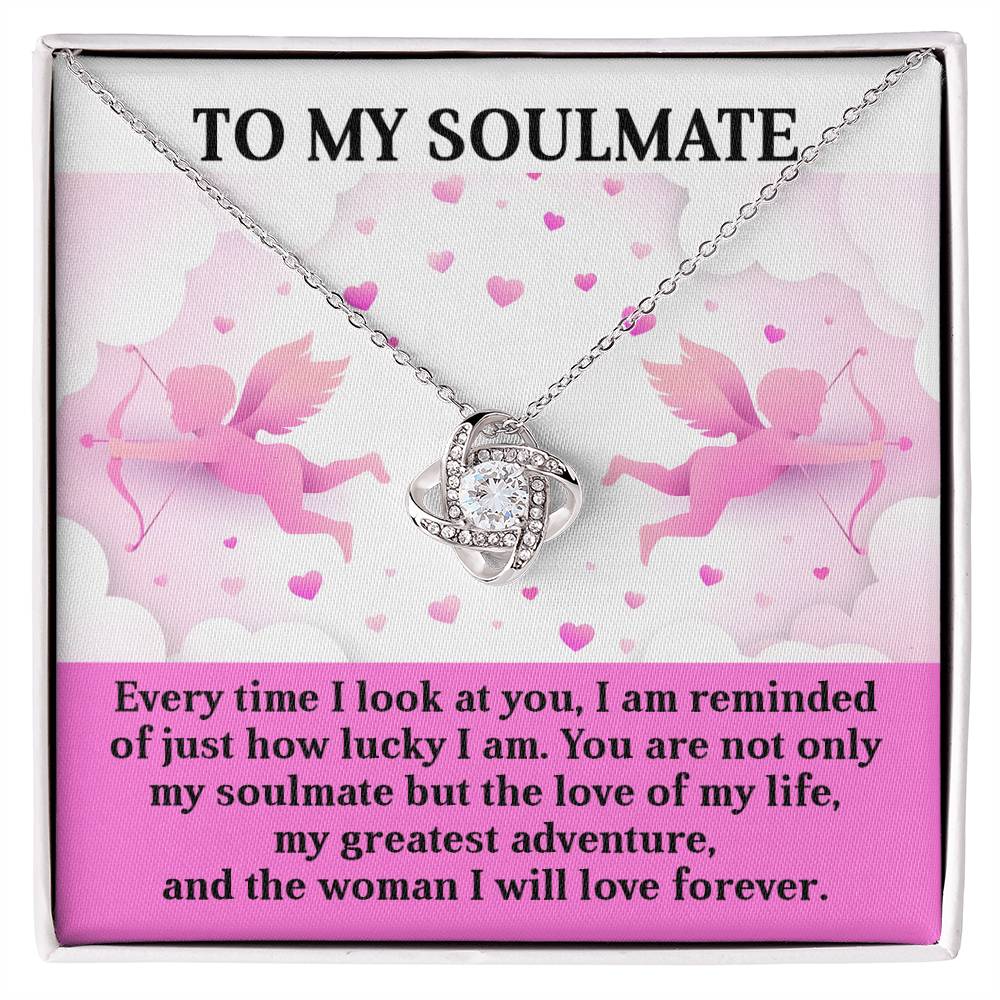 The Soulmate-Greatest Adventure Love Knot Necklace is crafted in 14k white gold with a shimmering cubic zirconia pendant, set against pink cherubs and hearts. The text reads: "To my soulmate. Every time I look at you, I'm reminded of just how lucky I am...