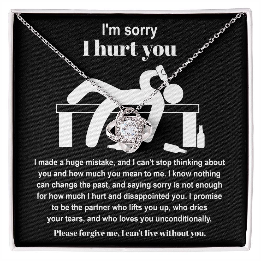 The Sorry-Change The Past 2 - Love Knot Necklace, featuring a pendant adorned with cubic zirconia crystals, is gracefully showcased on black fabric. It includes an apology message addressing past hurt and a heartfelt plea for forgiveness, complemented by illustrations of a distressed figure.