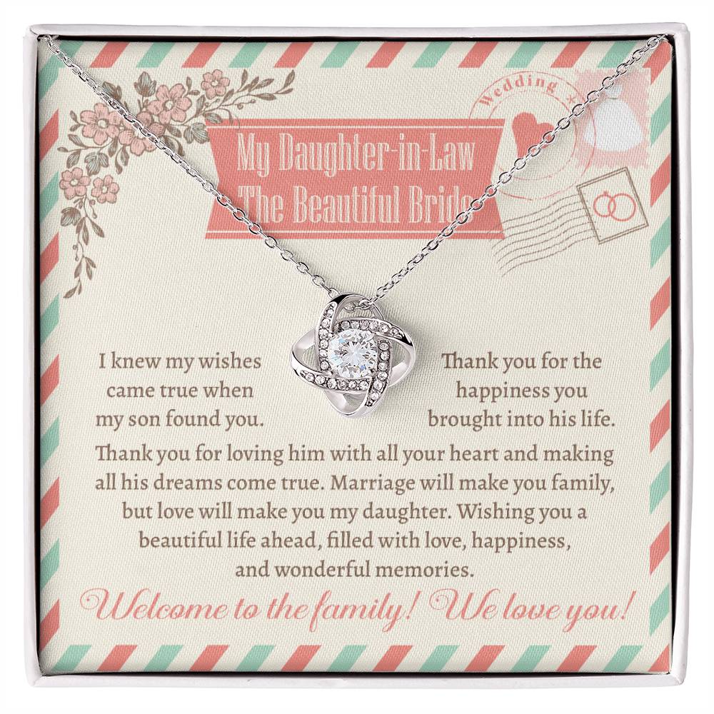 A "To My Daughter-In-Law, Make You Family - Love Knot Necklace" with an intertwined design is displayed on a heartfelt message card for a daughter-in-law, expressing love and welcoming her to the family. The piece, available in white gold or yellow gold finish, is adorned with shimmering cubic zirconia.