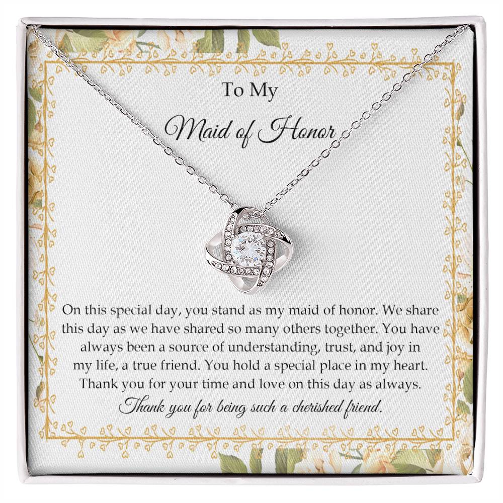 Presenting the "To Maid of Honor, Share This Day - Love Knot Necklace," featuring a stunning pendant adorned with cubic zirconia crystals and finished in white gold. It is beautifully displayed in a box embellished with a floral border and includes a heartfelt message expressing gratitude and appreciation to the "Maid of Honor.