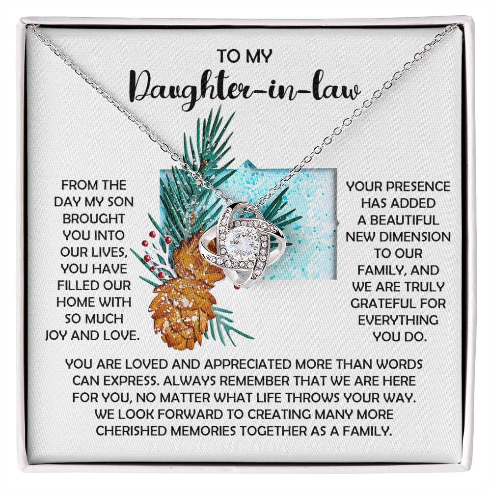 The Daughter-in-Law-Here For You - Love Knot Necklace, crafted in silver and featuring a shimmering cubic zirconia crystal pendant, is elegantly displayed on a gift card that includes heartfelt messages for a daughter-in-law, embellished with illustrations of pinecones and pine leaves.