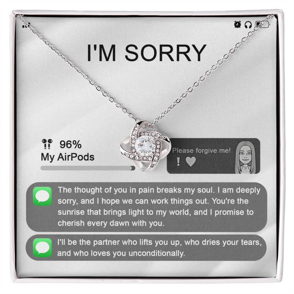 The "Sorry-Breaks My Soul - Love Knot Necklace" is a silver necklace featuring a pendant, beautifully displayed in its packaging. The front of the packaging includes a heartfelt apology message, text messages, a battery icon showing 96% for AirPods, and an illustrated figure. This intricately crafted piece is made from 14k white gold and adorned with cubic zirconia crystals.