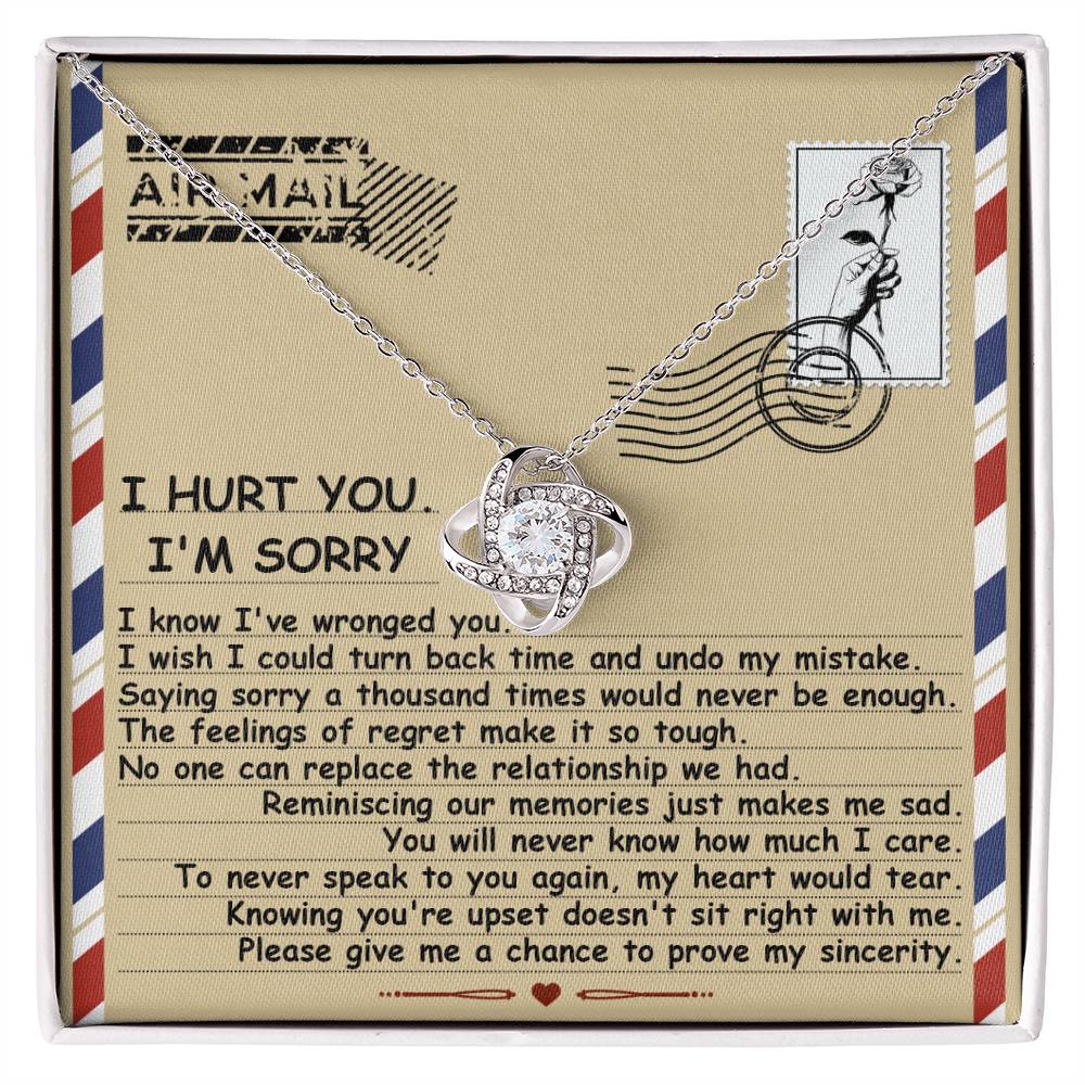 The Sorry-Makes Me Sad - Love Knot Necklace comes in a box and features a heart-shaped pendant adorned with cubic zirconia crystals set in a stunning gold finish. It includes an envelope-themed note expressing regret and asking for forgiveness, complete with heartfelt text and an "Air Mail" graphic at the top.