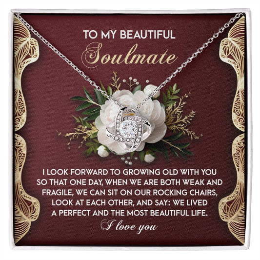 The Soulmate-Rocking Chairs Love Knot Necklace in white gold features a floral design with cubic zirconia, displayed on a red card with gold accents and a heartfelt message about love and growing old together.