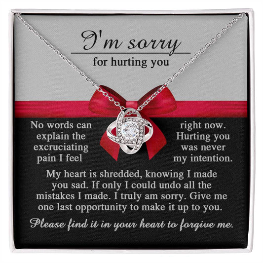 A "Sorry-Made You Sad - Love Knot Necklace" in a box with a red bow. The box, with its white gold finish, carries an apology message expressing regret for causing pain and asking for forgiveness.