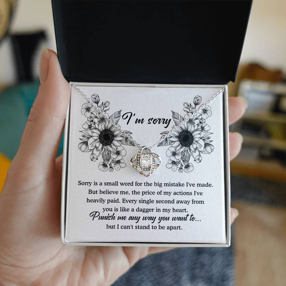 The "Sorry-Small Word - Love Knot Necklace" is a jewelry gift box that comes with an apology message. Inside, it contains a beautiful Love Knot Necklace featuring a silver pendant designed to resemble intertwined hearts, adorned with cubic zirconia crystals. The heartfelt message expresses deep regret and asks for forgiveness.