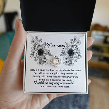 The "Sorry-Small Word - Love Knot Necklace" is a jewelry gift box that comes with an apology message. Inside, it contains a beautiful Love Knot Necklace featuring a silver pendant designed to resemble intertwined hearts, adorned with cubic zirconia crystals. The heartfelt message expresses deep regret and asks for forgiveness.