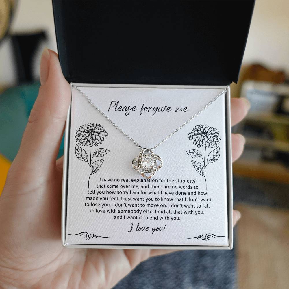 The Sorry-Real Explanation - Love Knot Necklace features an intertwined heart pendant adorned with cubic zirconia crystals, presented in a box. The box lid includes an apology note with floral illustrations, expressing regret, love, and a plea for forgiveness.