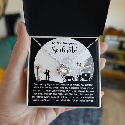 A hand opens a box to reveal the Soulmate-Holds For Us - Love Knot Necklace adorned with cubic zirconia crystals. The lid shows a heartfelt message for a "gorgeous soulmate," with a couple and carriage silhouette, making it the perfect personalized gift.