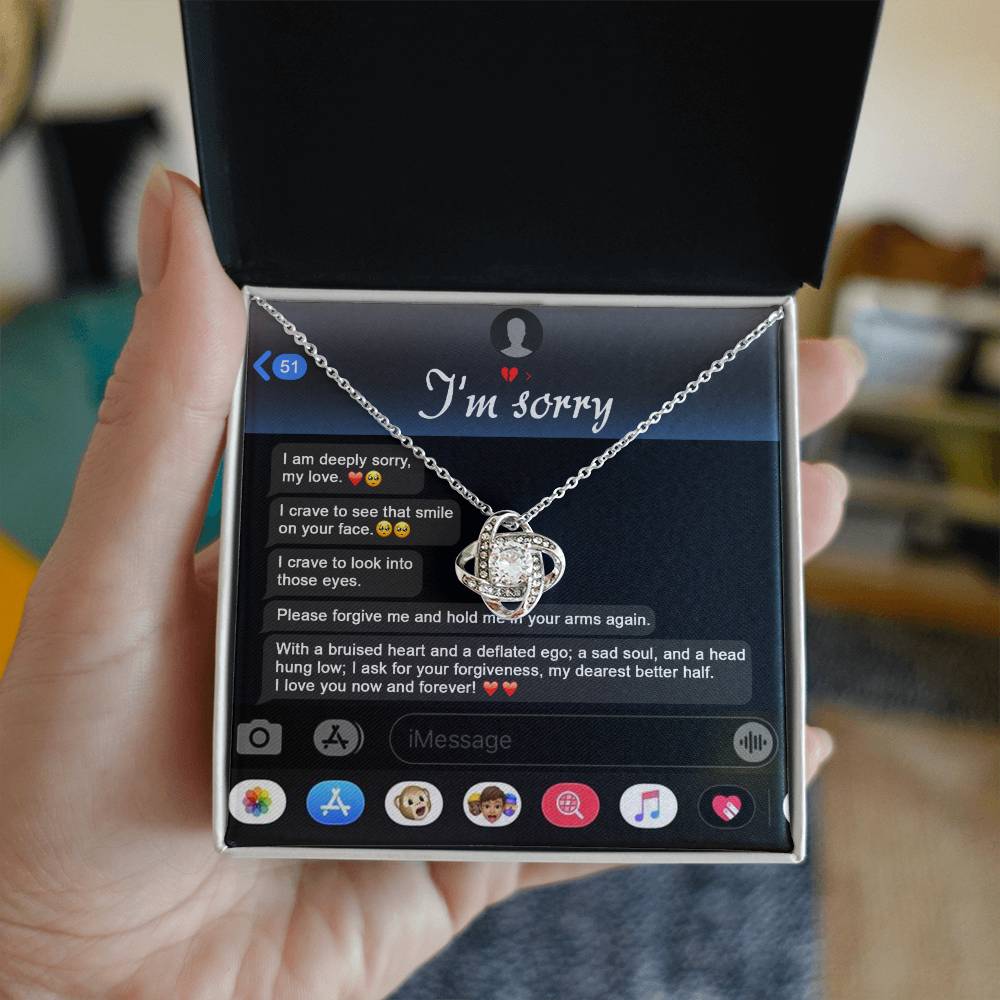 An "I'm sorry" message is displayed on a phone screen along with the stunning Sorry, Rebuild Our Connection - Love Knot Necklace. This necklace, available in either white gold or yellow gold finish and adorned with cubic zirconia crystals, perfectly complements the heartfelt plea for forgiveness.