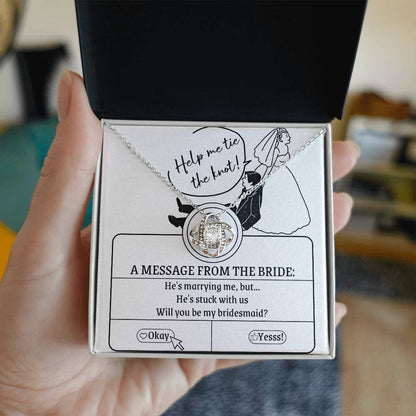 A To My Bridesmaid, Stuck With Us - Love Knot Necklace rests on a card that reads, "Help me tie the knot! A message from the bride: He's marrying me, but... He's stuck with us. Will you be my bridesmaid?