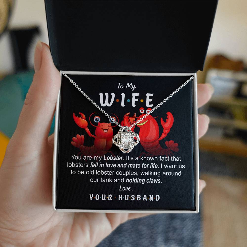 To Wife, Old Lobster Couples - Love Knot Necklace with a heart pendant displayed on a card featuring two cartoon lobsters and a message to a wife, discussing lifelong lobster mates and expressing love from a husband. The necklace sparkles with cubic zirconia crystals, symbolizing the unbreakable bond of your love.