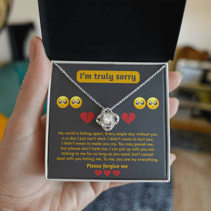 A hand holds an open box containing the "Sorry-Make You Cry - Love Knot Necklace" with a heart-shaped cubic zirconia pendant and an apologetic message that reads, "I'm truly sorry. Please forgive me." The text is decorated with emoji faces and hearts.