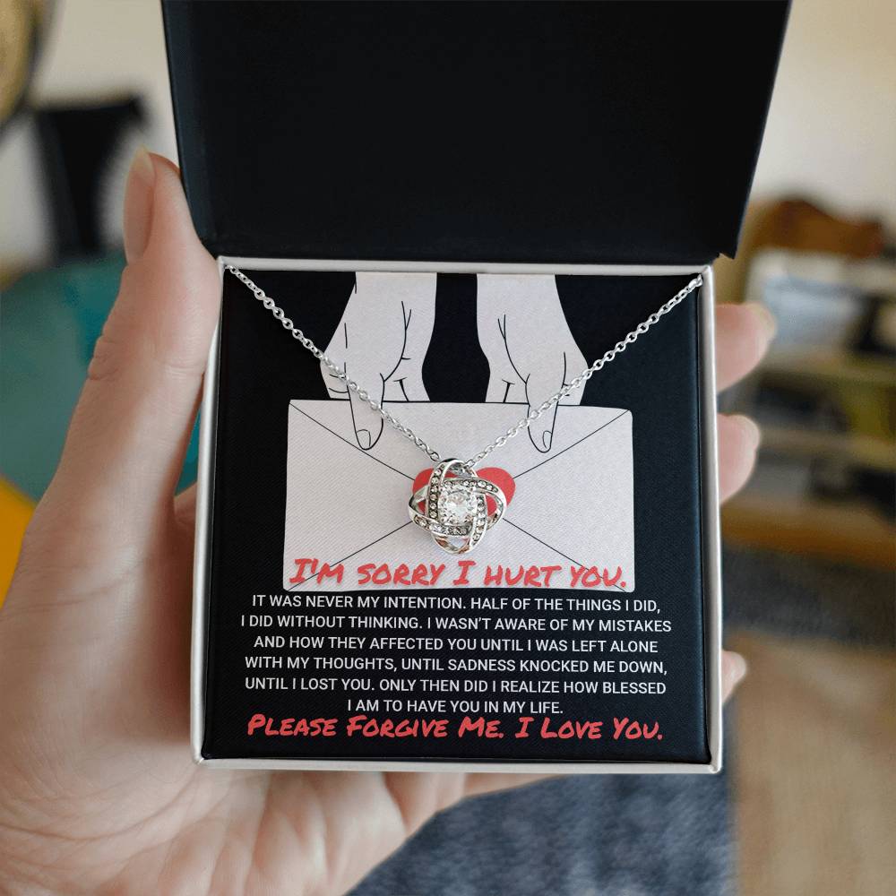 A hand holds an open gift box containing a stunning "Sorry-Without Thinking - Love Knot Necklace" adorned with cubic zirconia and a heartfelt message card apologizing for past mistakes and asking for forgiveness.