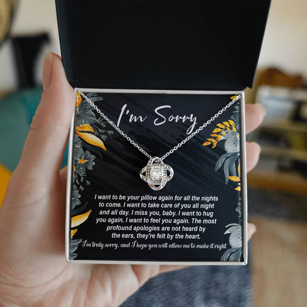 The "Sorry, Be Your Pillow - Love Knot Necklace" features an intertwined heart pendant adorned with cubic zirconia crystals. It comes in a gift box inscribed with "I'm Sorry" and includes a heartfelt apology message expressing regret and a desire for reconciliation.