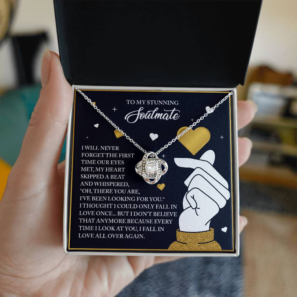 A person holds an open jewelry box featuring the Soulmate-Look At You - Love Knot Necklace with cubic zirconia crystals. The pendant, with a gleaming white gold finish, is displayed next to a romantic message and a hand-drawn finger heart gesture inside the box lid.
