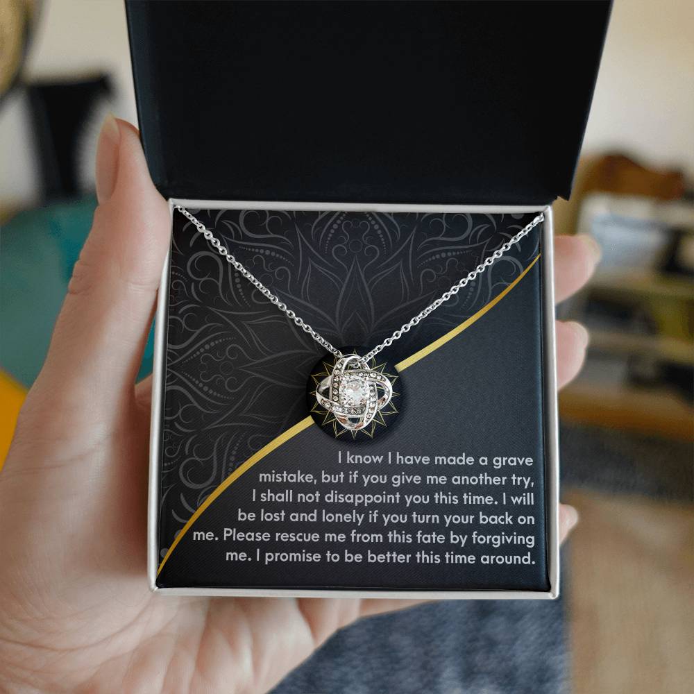 A hand holds an open box displaying a Sorry-Turn Your Back - Love Knot Necklace. The box's interior features an engraved message expressing regret and a plea for forgiveness, making it a heartfelt personalized gift.