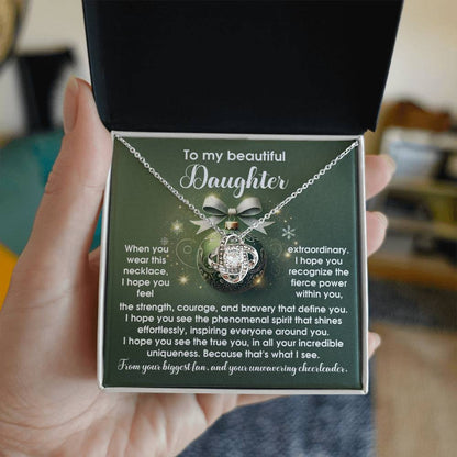 A hand holds an open jewelry box showcasing the "Daughter-Incredible Uniqueness - Love Knot Necklace," featuring a globe pendant. The box lid includes an inspirational message for a daughter, making it an ideal personalized gift.