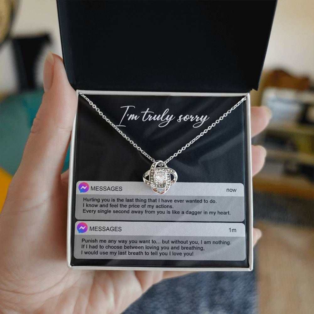 The Sorry-Away From You - Love Knot Necklace features interwoven heart pendants adorned with cubic zirconia crystals, and comes in a box with "I'm truly sorry" inscribed above. Accompanying the necklace are two text message excerpts expressing regret and love, making it an ideal personalized gift.