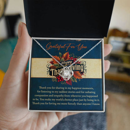 A hand holds an open box containing the Thanksgiving-Happiest Moments - Love Knot Necklace, beautifully adorned with Cubic Zirconia, and accompanied by a card that reads "Grateful for You" with a Thanksgiving theme featuring autumn leaves, making it the perfect personalized gift to express your gratitude.