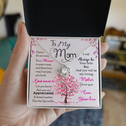 A hand holding a gift box with the "To My Mom, I Know Its Not Easy" Love Knot Necklace by ShineOn Fulfillment displayed inside.
