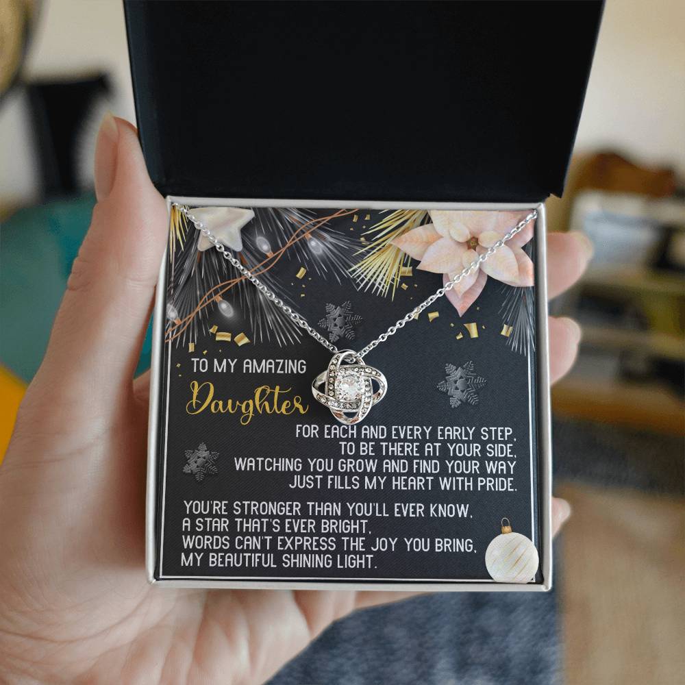 Introducing the Daughter-Shining Light - Love Knot Necklace, elegantly presented in a decorative box. This gift includes a silver heart pendant embellished with cubic zirconia crystals. The charming black background is adorned with floral and butterfly designs, making it the perfect personalized gift complete with a heartfelt message for your daughter.