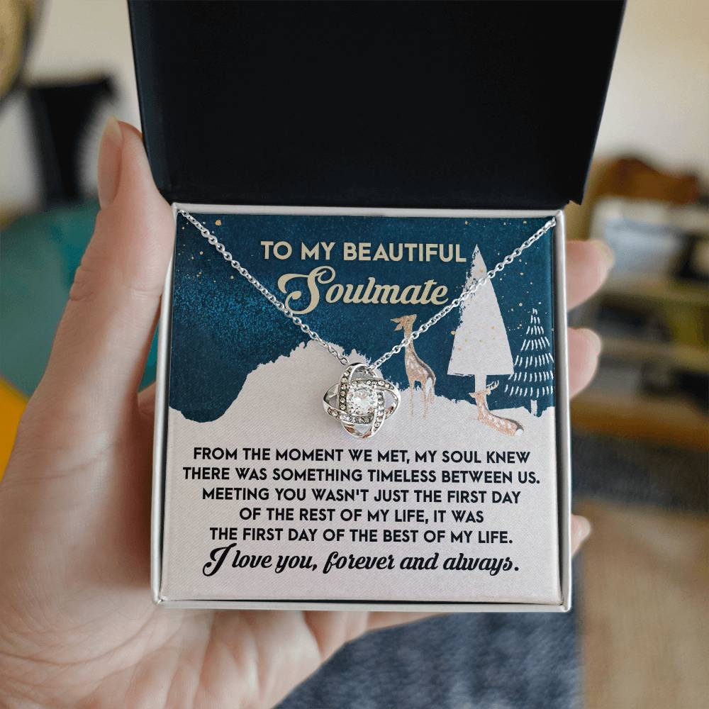 A hand holds an open black jewelry box featuring the "Soulmate- Between Us - Love Knot Necklace." Inside, the box contains a heartfelt message dedicated to a soulmate, expressing love and a deep connection. The necklace is further enhanced by sparkling cubic zirconia crystals, adding extra charm to this personalized gift.