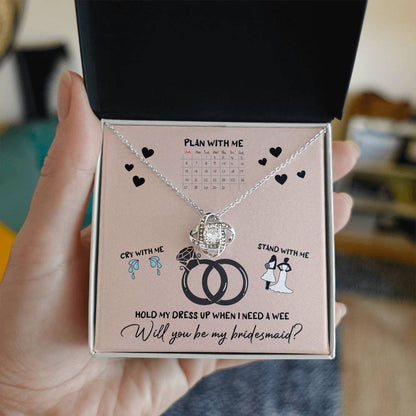 A To Bridesmaid, Will You Be 2 - Love Knot Necklace, adorned with cubic zirconia crystals, is displayed on a card featuring a calendar, wedding rings, and bridesmaid-related illustrations. The text reads, "Will you be my bridesmaid?" Choose from a white gold or yellow gold finish to make the moment even more special.