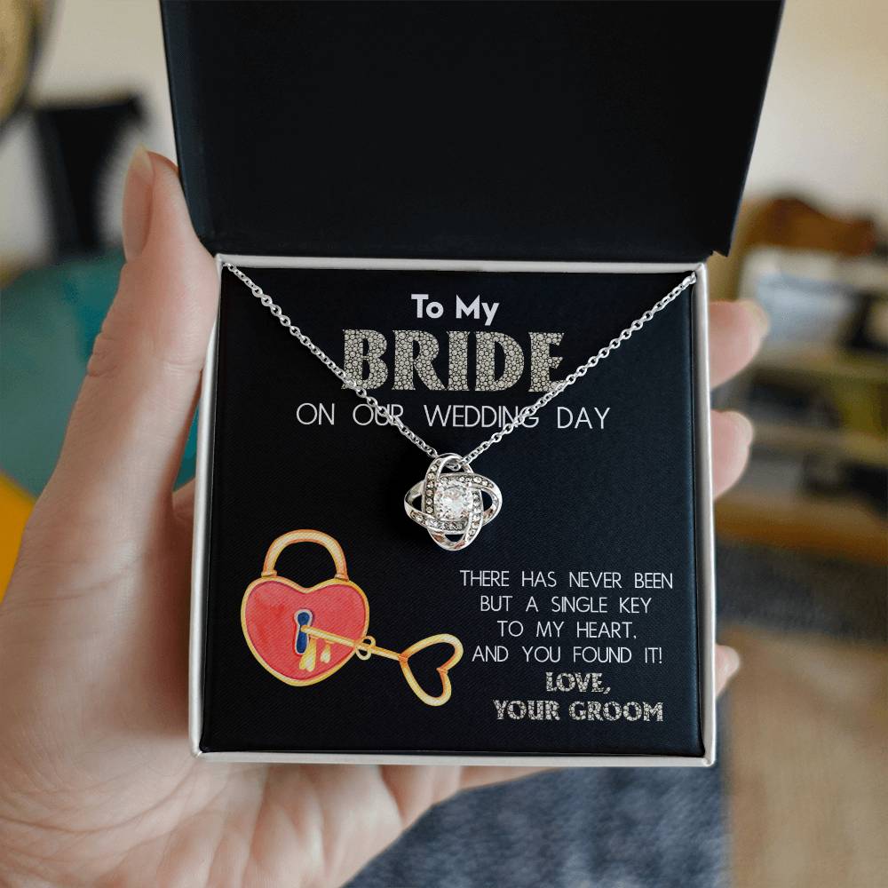 A "To My Bride, A Single Key - Love Knot Necklace" adorned with cubic zirconia crystals is displayed against a background with text that reads, "To My Bride On Our Wedding Day" and "There has never been but a single key to my heart, and you found it! Love, Your Groom.