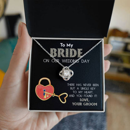 A "To My Bride, A Single Key - Love Knot Necklace" adorned with cubic zirconia crystals is displayed against a background with text that reads, "To My Bride On Our Wedding Day" and "There has never been but a single key to my heart, and you found it! Love, Your Groom.