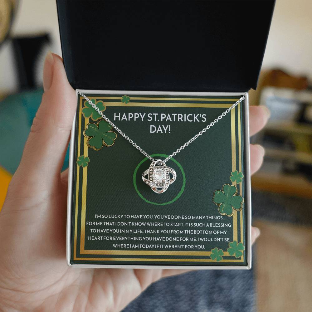 A hand holding a Happy St. Patrick Day, I'm So Lucky - Love Knot Necklace by ShineOn Fulfillment in a box.