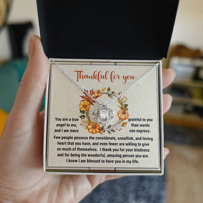 Close-up of a hand holding a necklace box containing the Thanksgiving-The Wonderful - Love Knot Necklace. The pendant, adorned with shimmering cubic zirconia crystals, is nestled below the box lid, which displays a heartfelt message expressing gratitude and appreciation.