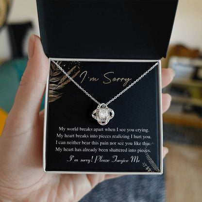 The Sorry-See You Crying - Love Knot Necklace, featuring an intertwined pendant adorned with cubic zirconia crystals, is elegantly displayed on a black card with the inscription "I'm Sorry" and an apology message in white text.