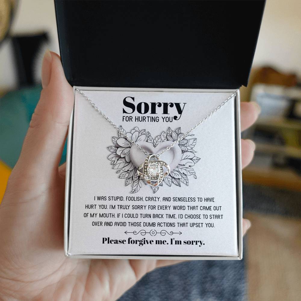 The Sorry-Turn Back Time - Love Knot Necklace, adorned with sparkling cubic zirconia crystals and featuring an intertwined pendant, is displayed on a card with the heartfelt apology message, "Sorry for hurting you," symbolizing an unbreakable bond and a request for forgiveness.