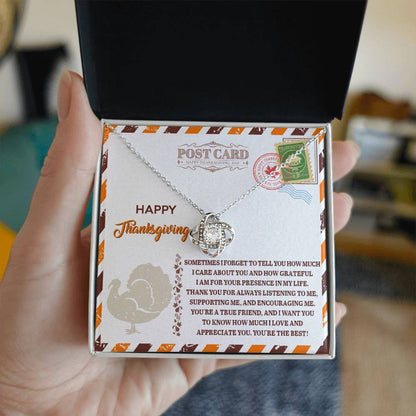 An open black gift box is held by a hand, showcasing the Thanksgiving-A True Friend - Love Knot Necklace embellished with sparkling cubic zirconia crystals. The necklace is elegantly displayed on a card featuring decorative Thanksgiving-themed text and designs, representing the enduring connection between cherished friends.