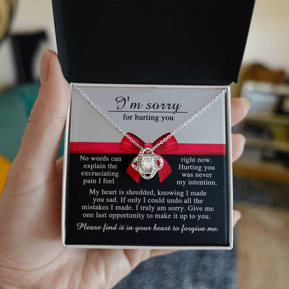 A hand holds an open gift box displaying a stunning Sorry-Made You Sad - Love Knot Necklace adorned with cubic zirconia crystals, accompanied by a heartfelt note that reads "I'm sorry for hurting you," expressing deep remorse and a plea for forgiveness.