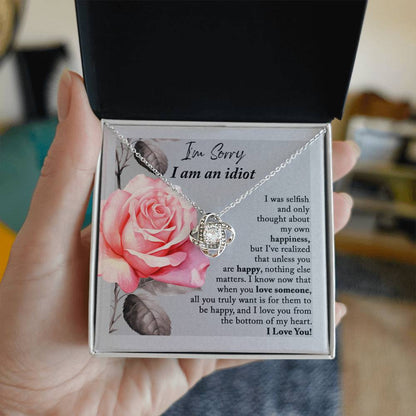 The "Sorry-Love Someone - Love Knot Necklace" is an elegant silver piece with a heart-shaped pendant, adorned with sparkling cubic zirconia crystals. It rests on a beautifully designed box featuring a pink rose and a heartfelt apology note, making it truly a classic gift.