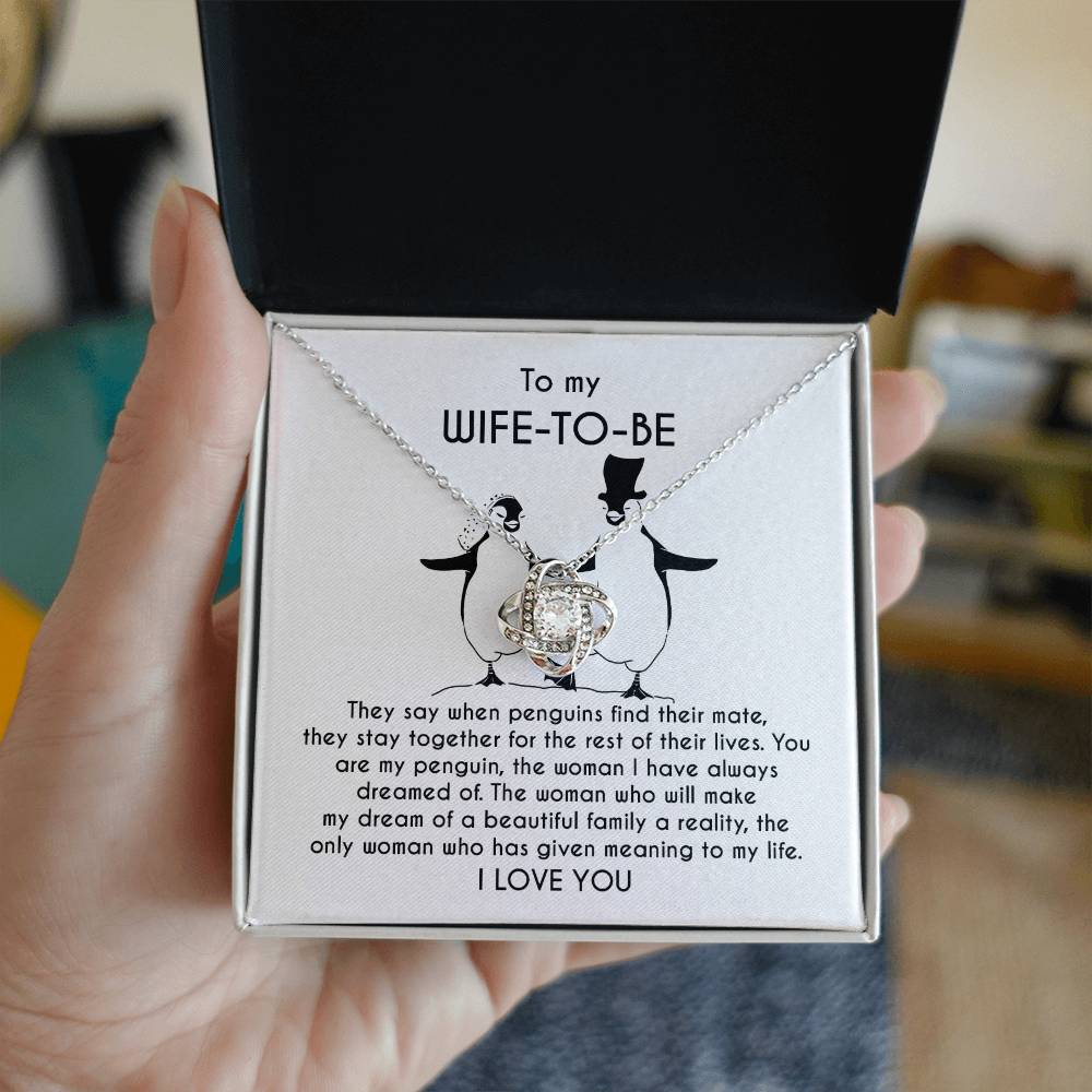 A silver *To Wife-to-be, My Penguin - Love Knot Necklace* with a flower-like pendant is displayed on a jewelry card. The card contains a message to a "Wife-To-Be" featuring a heartfelt dedication and illustrations of two penguins.