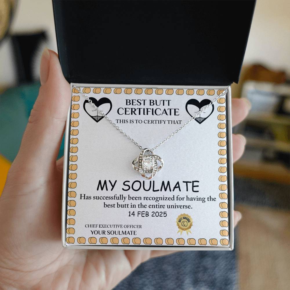 A hand displays an open box with the "Love Certificate-Best Butt - Love Knot Necklace" featuring cubic zirconia crystals and a comedic "Best Butt Certificate" for "My Soulmate," blending elegance and humor into a perfect personalized gift.