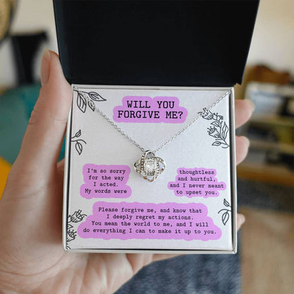 A hand holds an open black box containing a personalized gift: the "Sorry-Never Meant To - Love Knot Necklace" adorned with cubic zirconia crystals and a card that reads, "WILL YOU FORGIVE ME?" with an apology message beneath it.