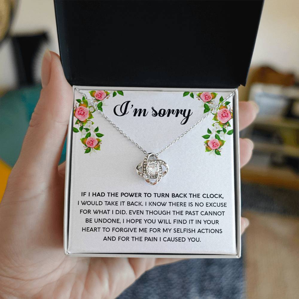 The "Sorry, Make It Right - Love Knot Necklace," featuring a silver intertwined knot pendant adorned with cubic zirconia crystals, is beautifully displayed in a box. The text on the box reads, "I’m sorry," with an apology message below, framed by a floral border in the top corners.