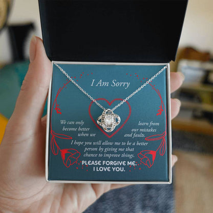 The Sorry-Mistakes And Faults - Love Knot Necklace, featuring a heart-shaped pendant with sparkling cubic zirconia set in white gold, is elegantly presented in a box adorned with the words "I Am Sorry" and a heartfelt apology message.