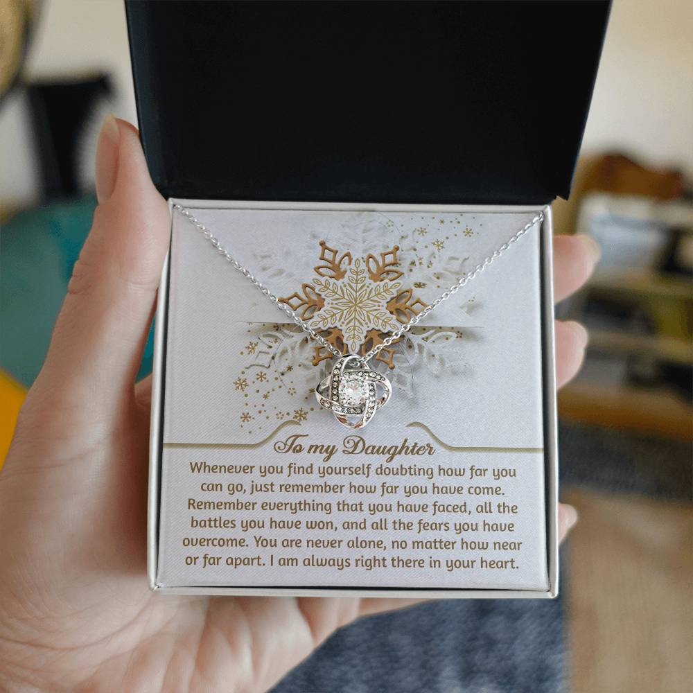 A hand opens the box to unveil a Daughter-You Can Go - Love Knot Necklace, adorned with dazzling cubic zirconia crystals. The box's lid carries an uplifting message for "To my Daughter," representing the enduring connection between you.