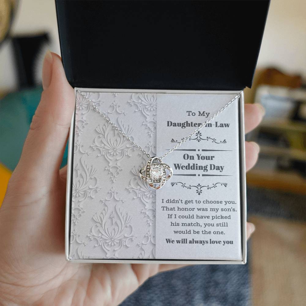 To My Daughter-In-Law Wedding, Be The One - Love Knot Necklace with an intertwined heart design, adorned with cubic zirconia crystals, displayed on a decorative backing card. The card reads: "To My Daughter-In-Law On Your Wedding Day" with a sentimental message below. Perfect as a gift for a loved one.