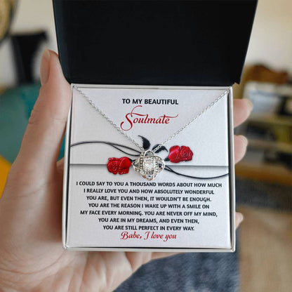 A hand presents the Soulmate-Every Morning Love Knot Necklace in White Gold Finish, featuring a heart design with Cubic Zirconia Crystals and delicate roses. The gift box includes a heartfelt soulmate message of love and admiration.